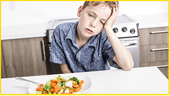 Ein Junge sitzt vor einem Teller mit Gemüse